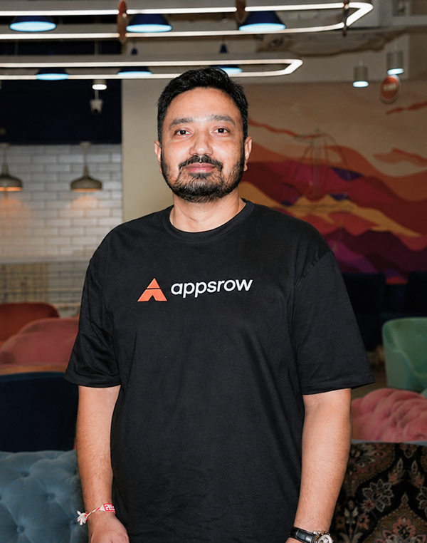 Man with beard and mustache wearing a black Appsrow T-shirt in a modern lounge setting.