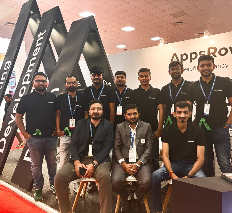 Group of ten men posing at an AppsRow booth at a tech event.
