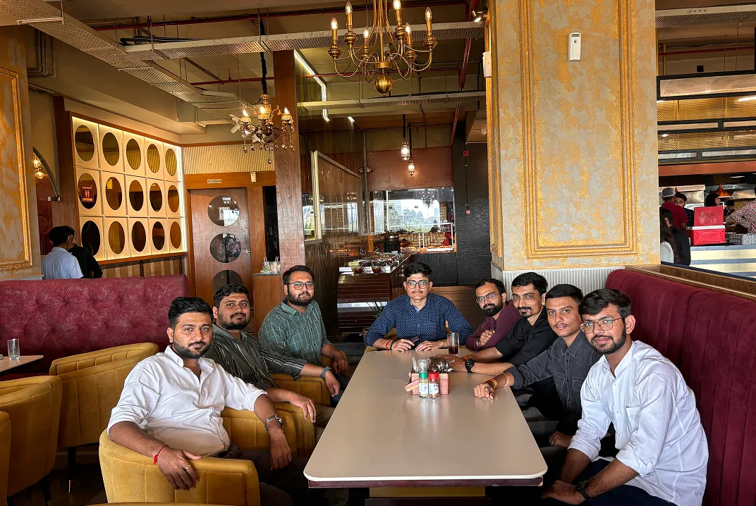 Group of nine men sitting around a restaurant table with chandeliers and decorated walls.