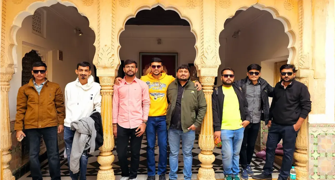 Eight men standing in front of ornate yellow archways with carved columns in a historic building.