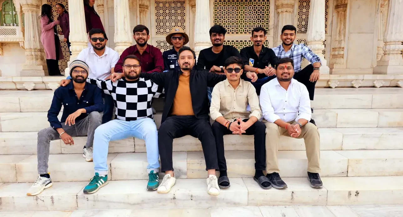 Group of 12 men sitting and standing on marble steps at an ornate building with carved pillars.