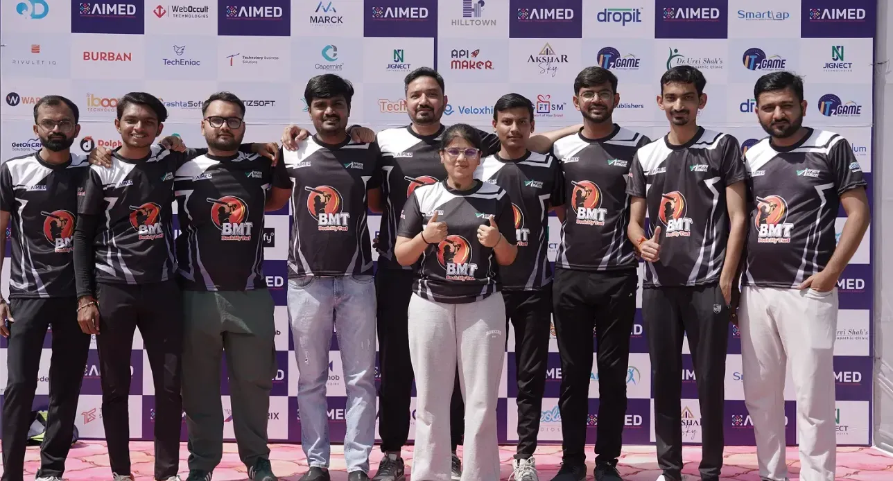 Group of ten people in matching black sports jerseys posing and smiling in front of a sponsor backdrop.
