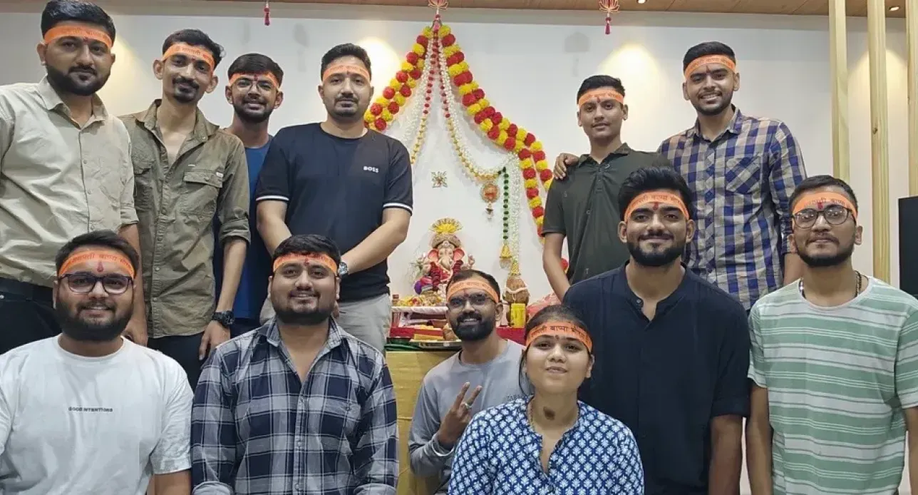Group of young people wearing orange headbands posing in front of a decorated Ganesh idol at a celebration.