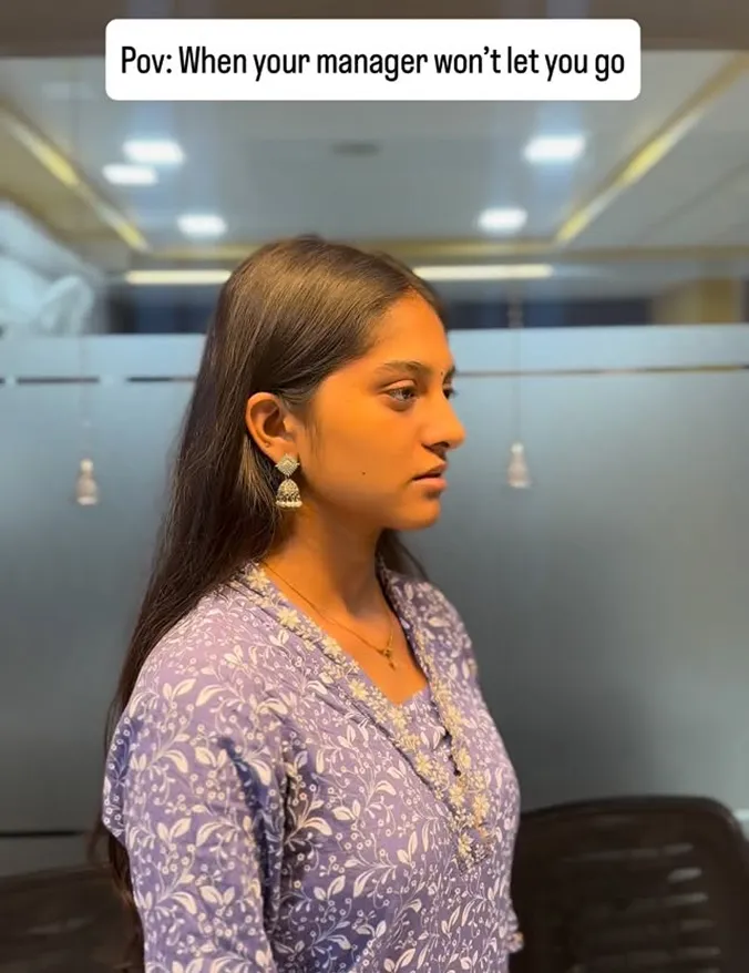 Woman in purple patterned dress looks sideways with a neutral expression in an office setting.