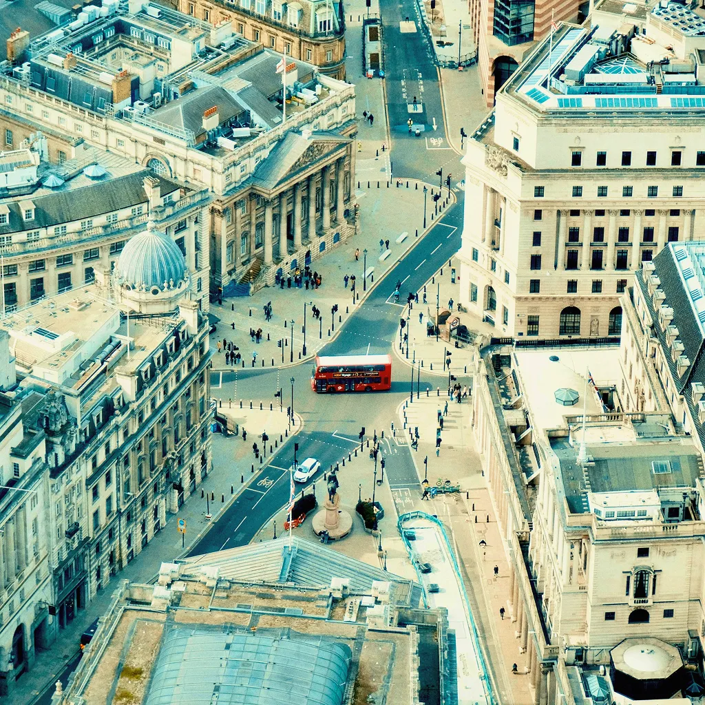 Aerial view of a city street with historic buildings and a red double-decker bus driving through.