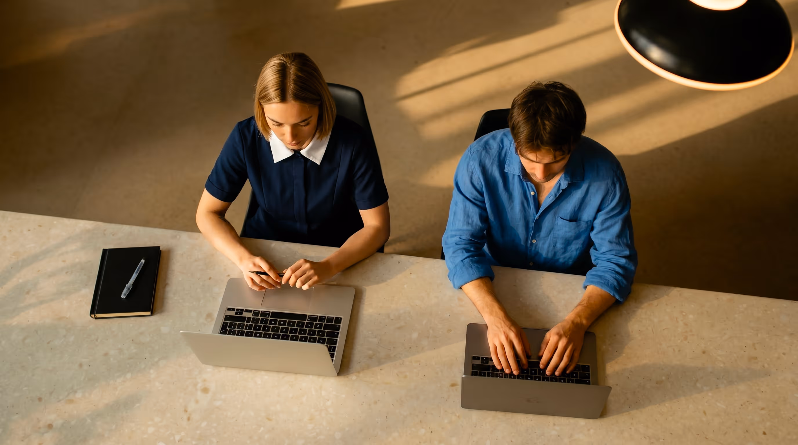 Two people sitting at a table with laptops.