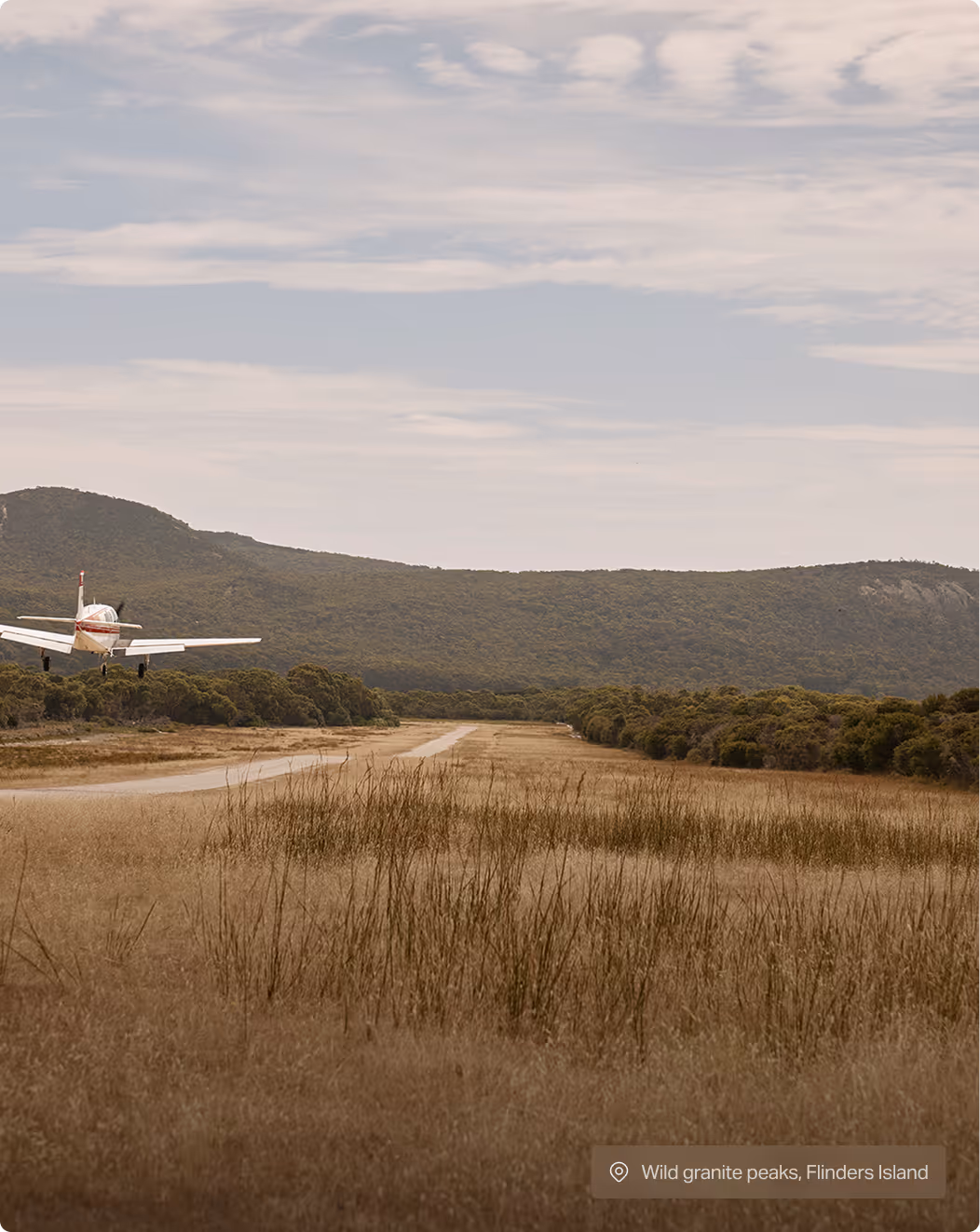 Small airplane landing on a runway surrounded by grass and trees with hills in the background.