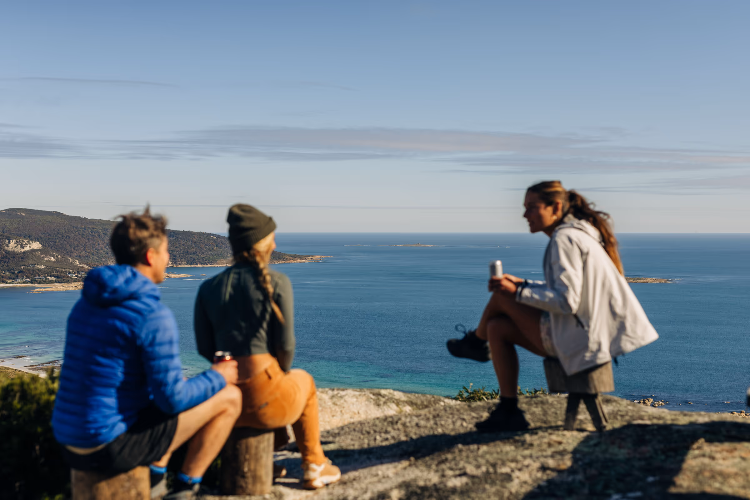 Three people sitting on rocks enjoying a coastal ocean view under a clear sky.