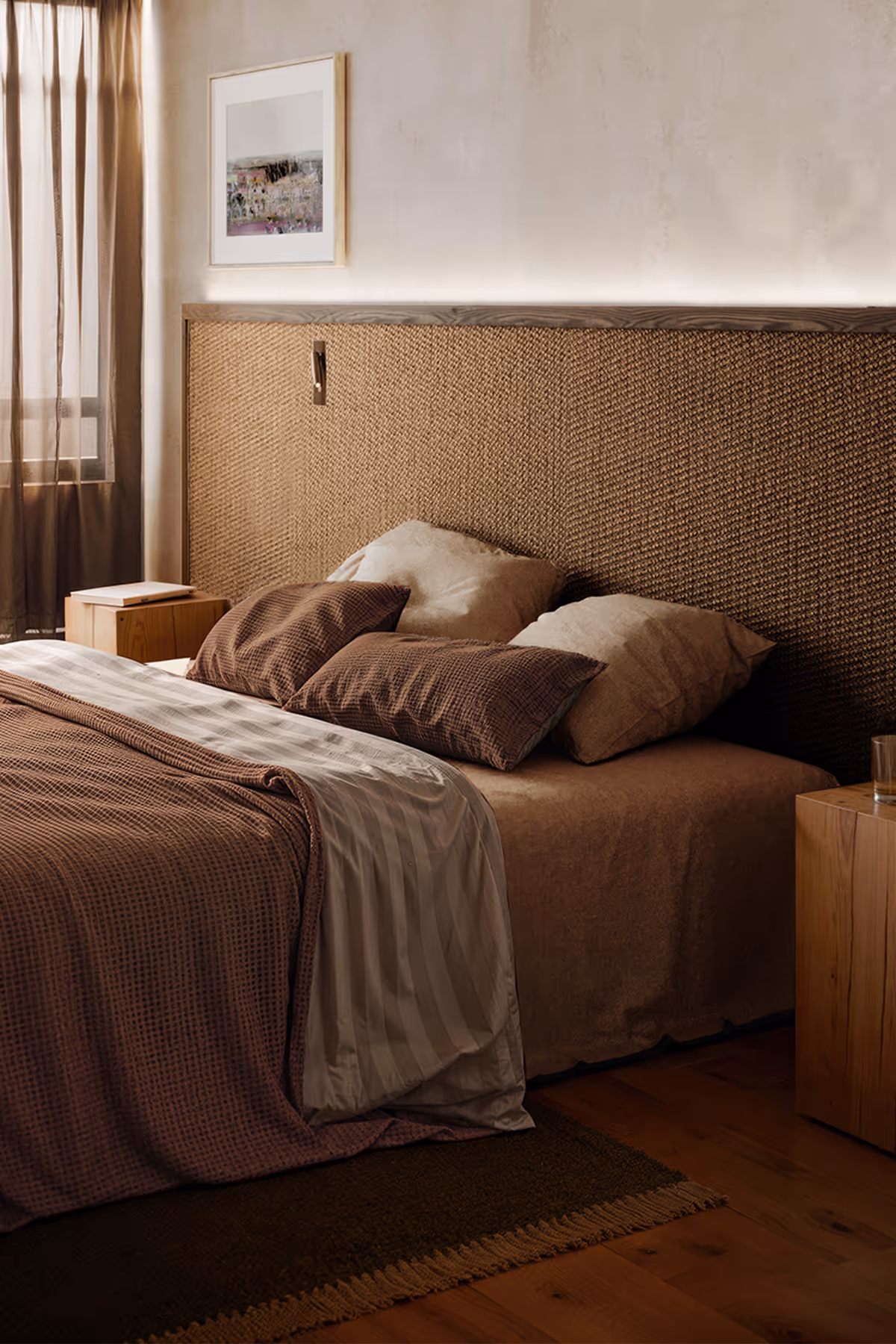 Cozy bedroom with brown bedding, woven headboard, wooden nightstands, sheer curtains, and framed artwork.