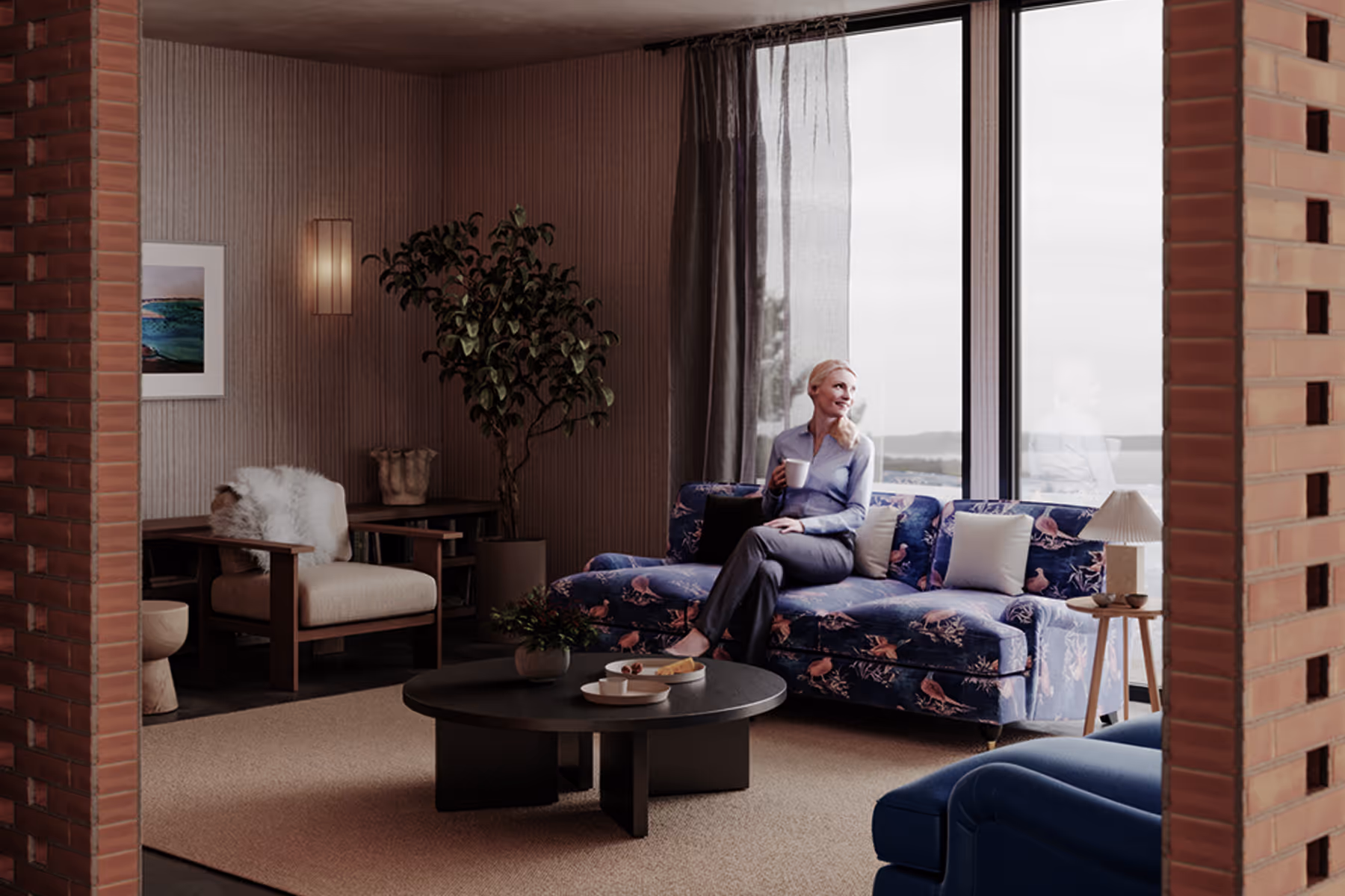 Woman holding cup sitting on a floral sofa in a cozy living room with large windows and soft lighting.