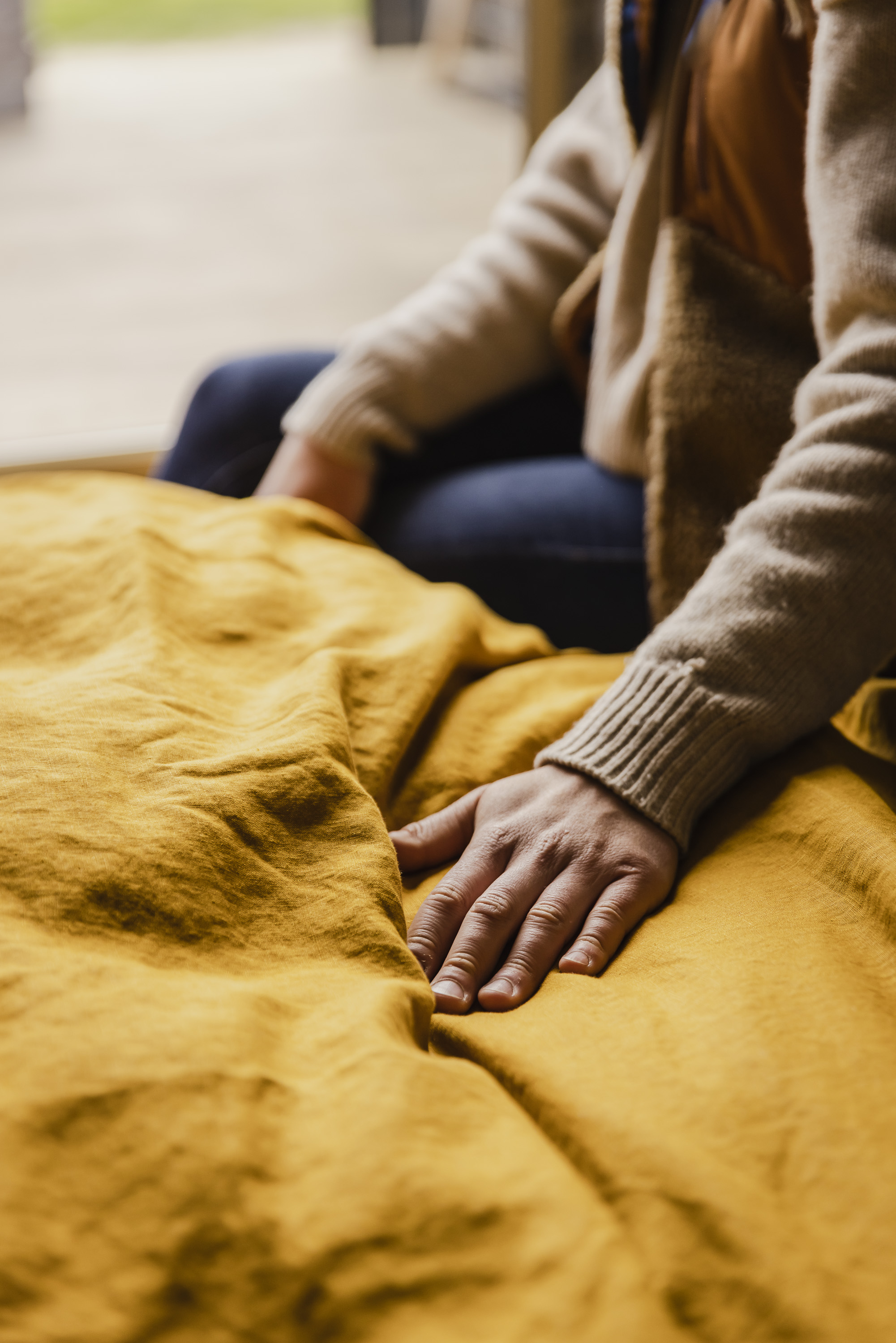 Person with beige sweater touching a wrinkled mustard yellow fabric.