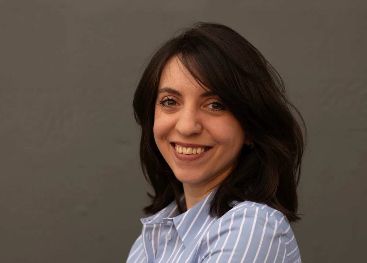 Clara Cristea, UX Designer, smiling in a striped shirt against a dark background