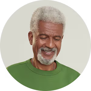 Smiling elderly man with gray hair and beard wearing a green shirt against a neutral background.