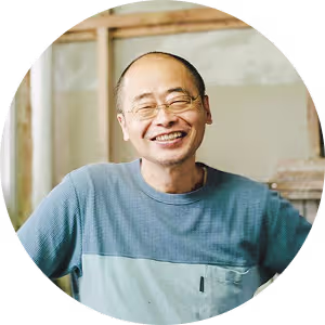 Smiling middle-aged man wearing glasses and a blue shirt, standing indoors with blurred background.