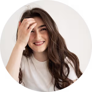 Smiling woman with long brown hair wearing a white shirt, touching her forehead.