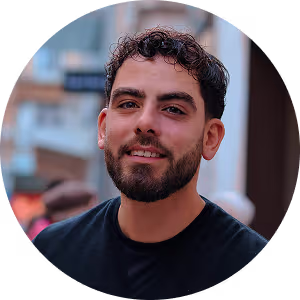 Portrait of a smiling man with curly hair and beard wearing a black shirt outdoors.