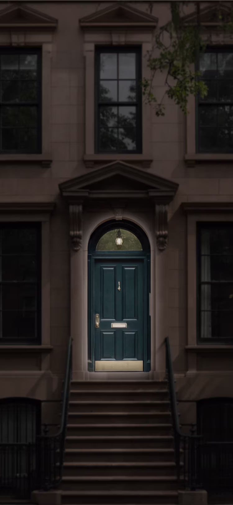 Dark blue front door with silver mail slot and door knocker, framed by stone steps and columns.