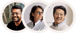 Three smiling business professionals: man with glasses and beard, woman with glasses, man with glasses and sweater.