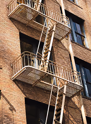Metal fire escape ladders and platforms on a brick apartment building with windows.