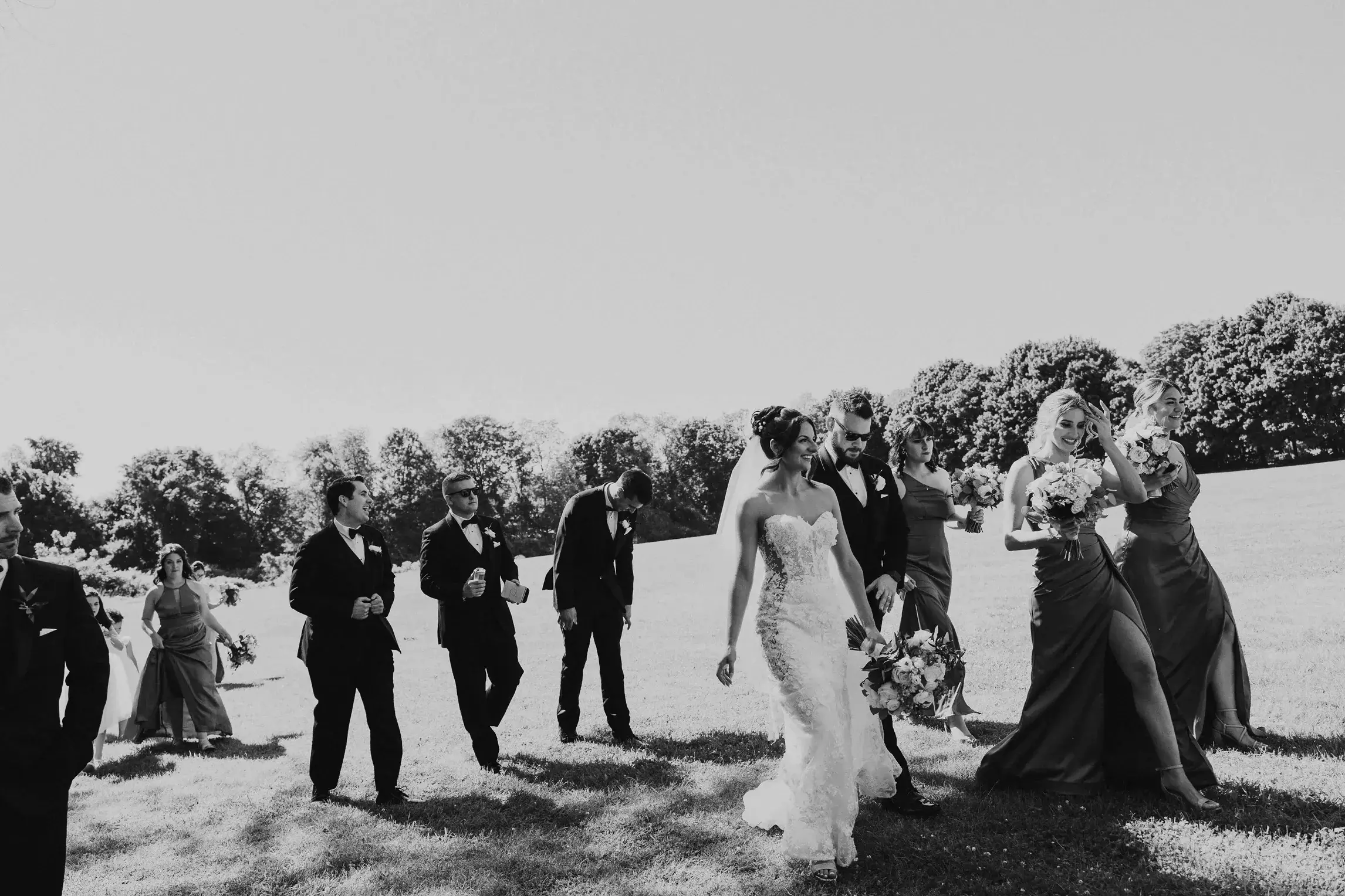 Bride and groom walking with their wedding party across a grassy lawn during an outdoor celebration at Wyndham Newport in Rhode Island, photographed by a New England wedding photographer.