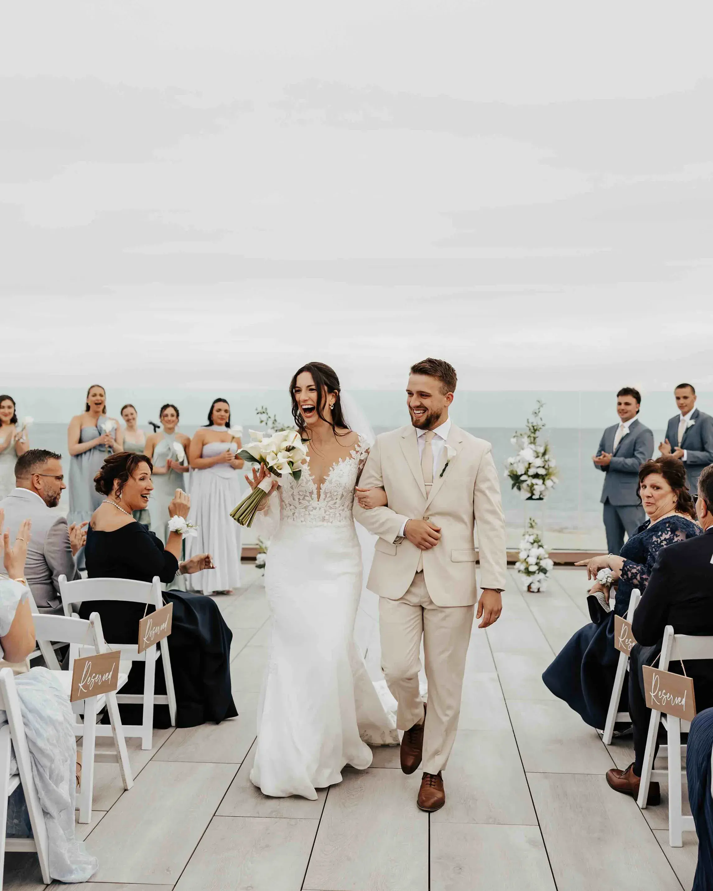 Bride and groom celebrating their Cape Cod wedding as they walk down the aisle together at the Wychmere Club in Harwich, Massachusetts, with the ocean and New England coast in the background.