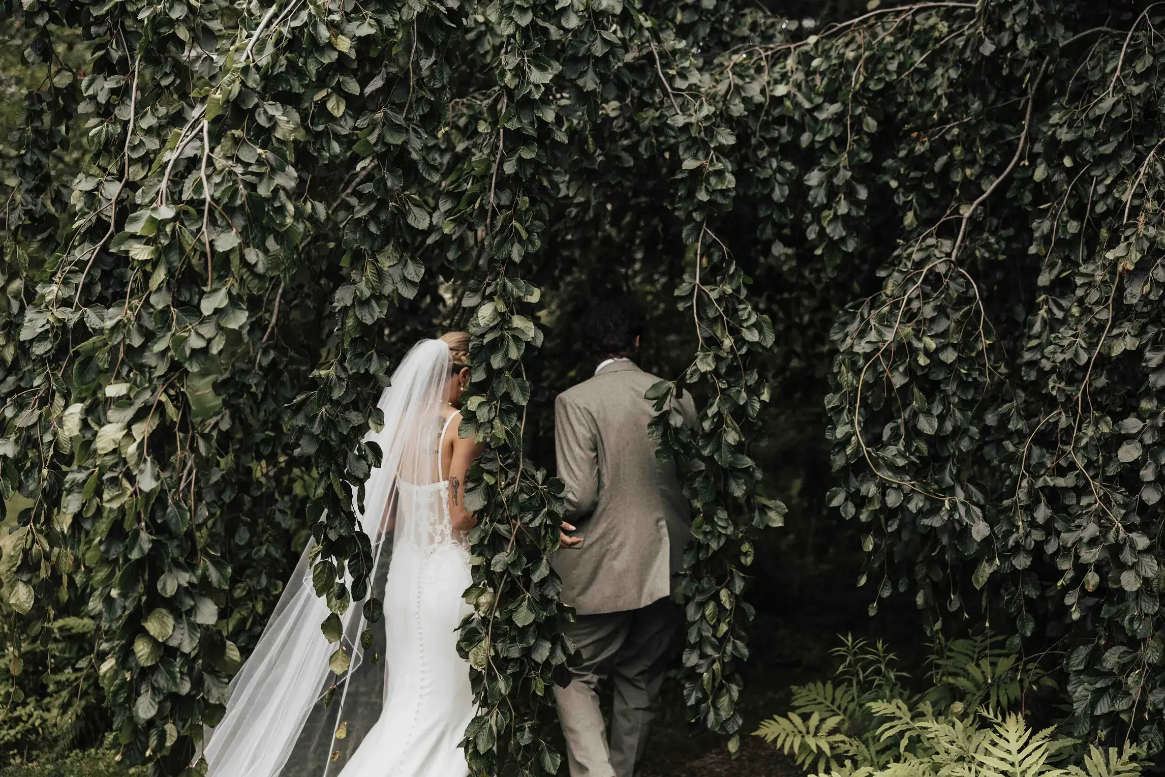 Bride and groom walking beneath the cascading trees at Glen Magna Farms in Danvers, Massachusetts, during a quiet moment captured by a wedding photographer.