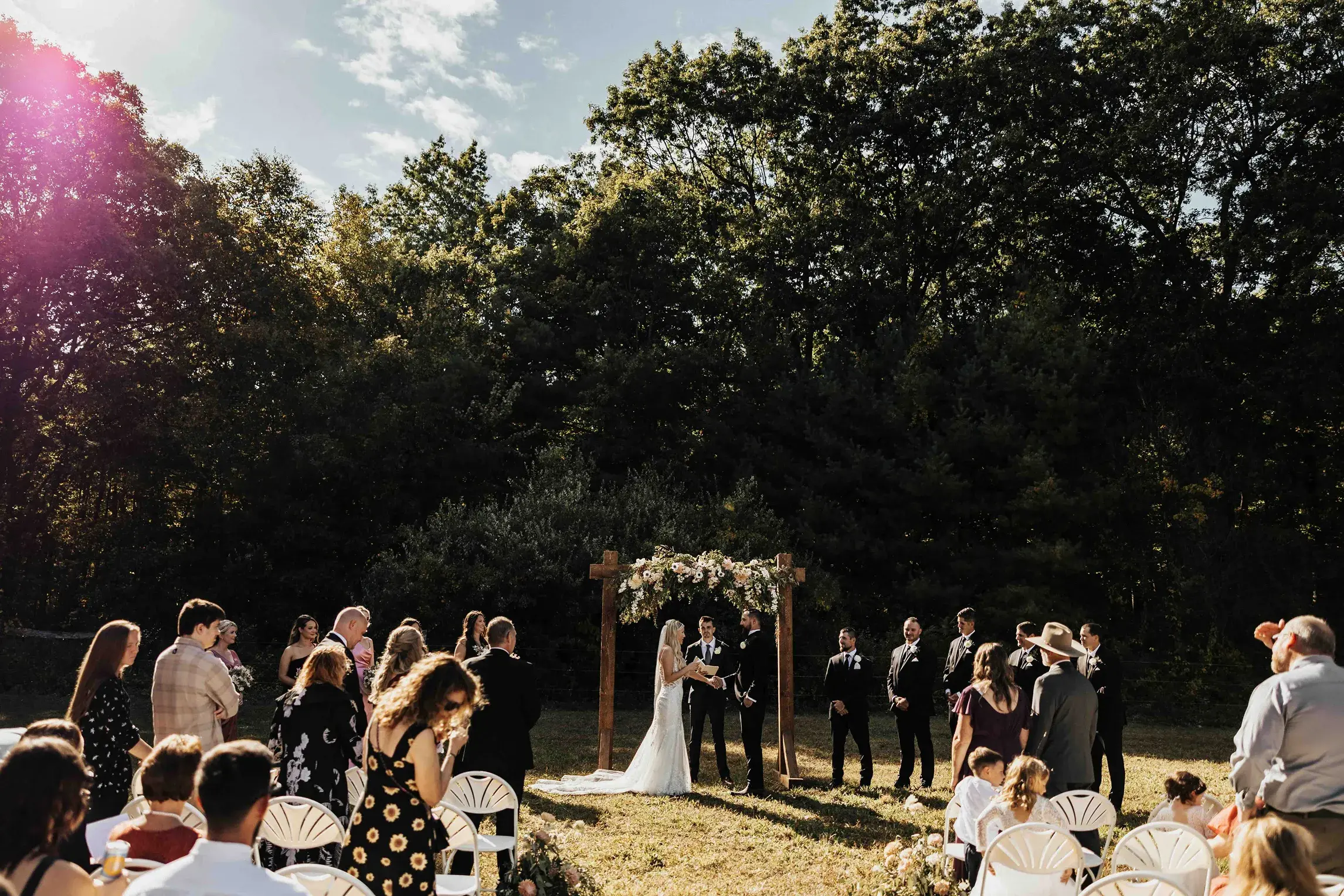 Bride and groom exchanging vows beneath a floral arbor during a backyard wedding ceremony in Southwick, Western Massachusetts, surrounded by family and friends.