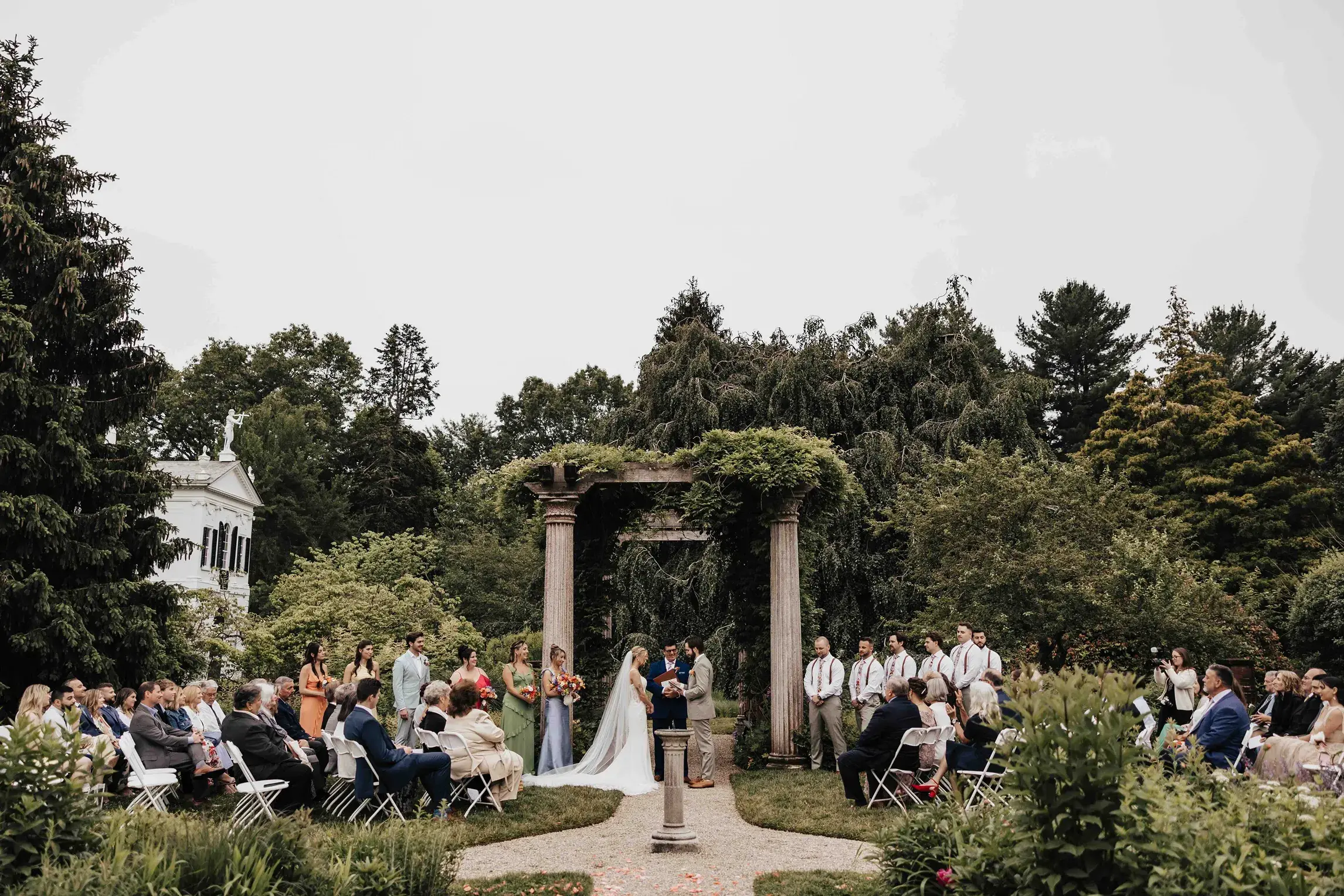 Bride and groom exchanging vows during an outdoor wedding ceremony at Glen Magna Farms in Massachusetts, surrounded by family and friends in a beautifully landscaped garden near Boston.