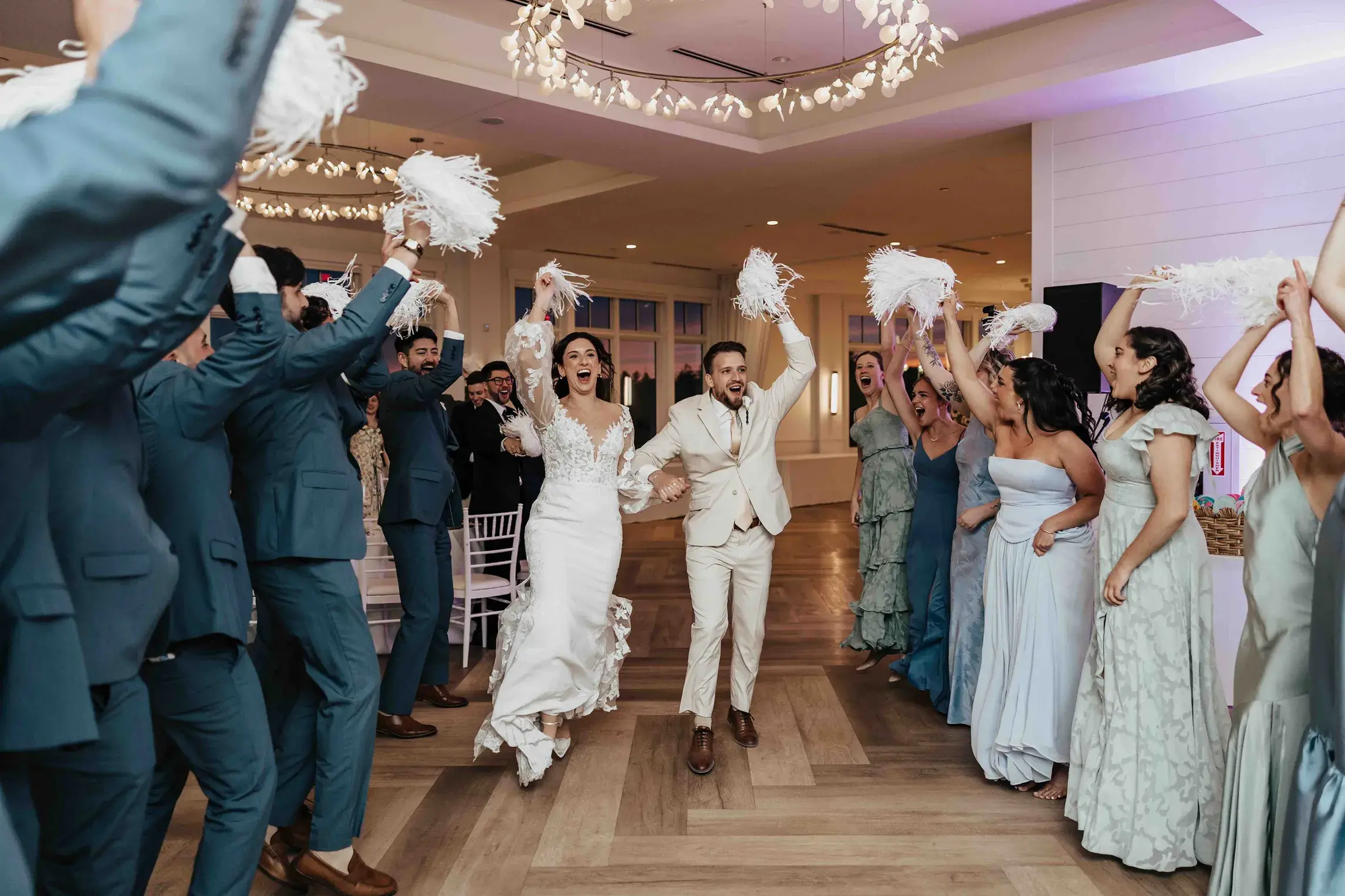 Bride and groom making their grand entrance into the reception at Wychmere Beach Club in Harwich, Cape Cod, as family and friends cheer them on with white pom-poms.