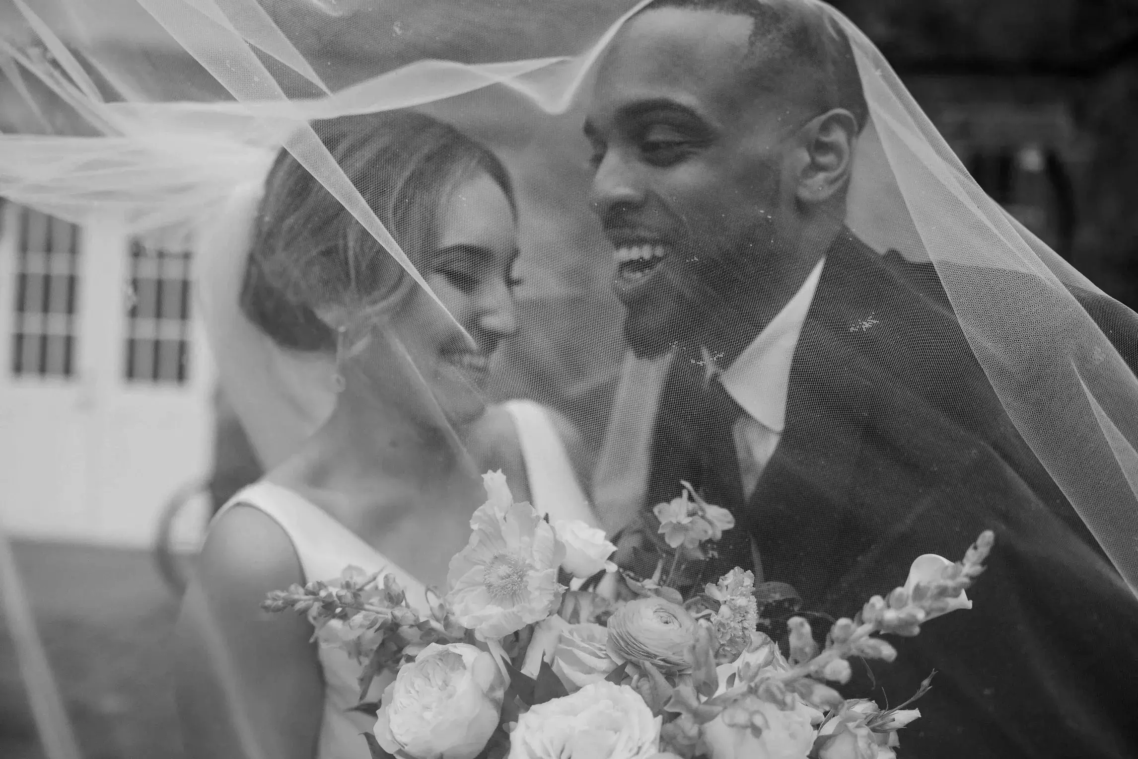 Bride and groom sharing a joyful moment beneath the bride's veil after their wedding at The White Room in Worcester, Massachusetts, with a bouquet of fresh blooms in the foreground.