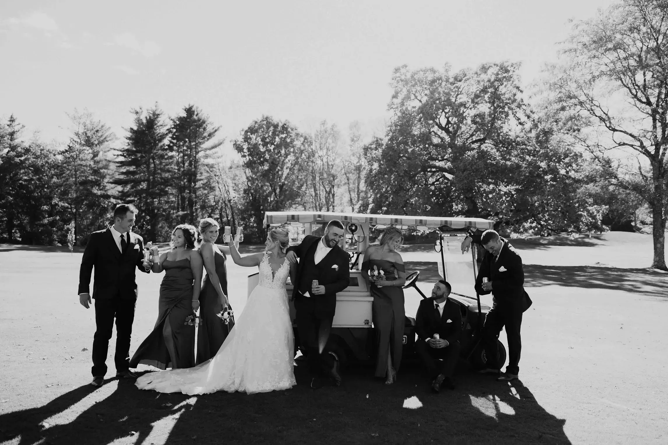Bride, groom, and their wedding party celebrating beside a golf cart on a country club golf course in Massachusetts, sharing drinks and laughter after the ceremony.