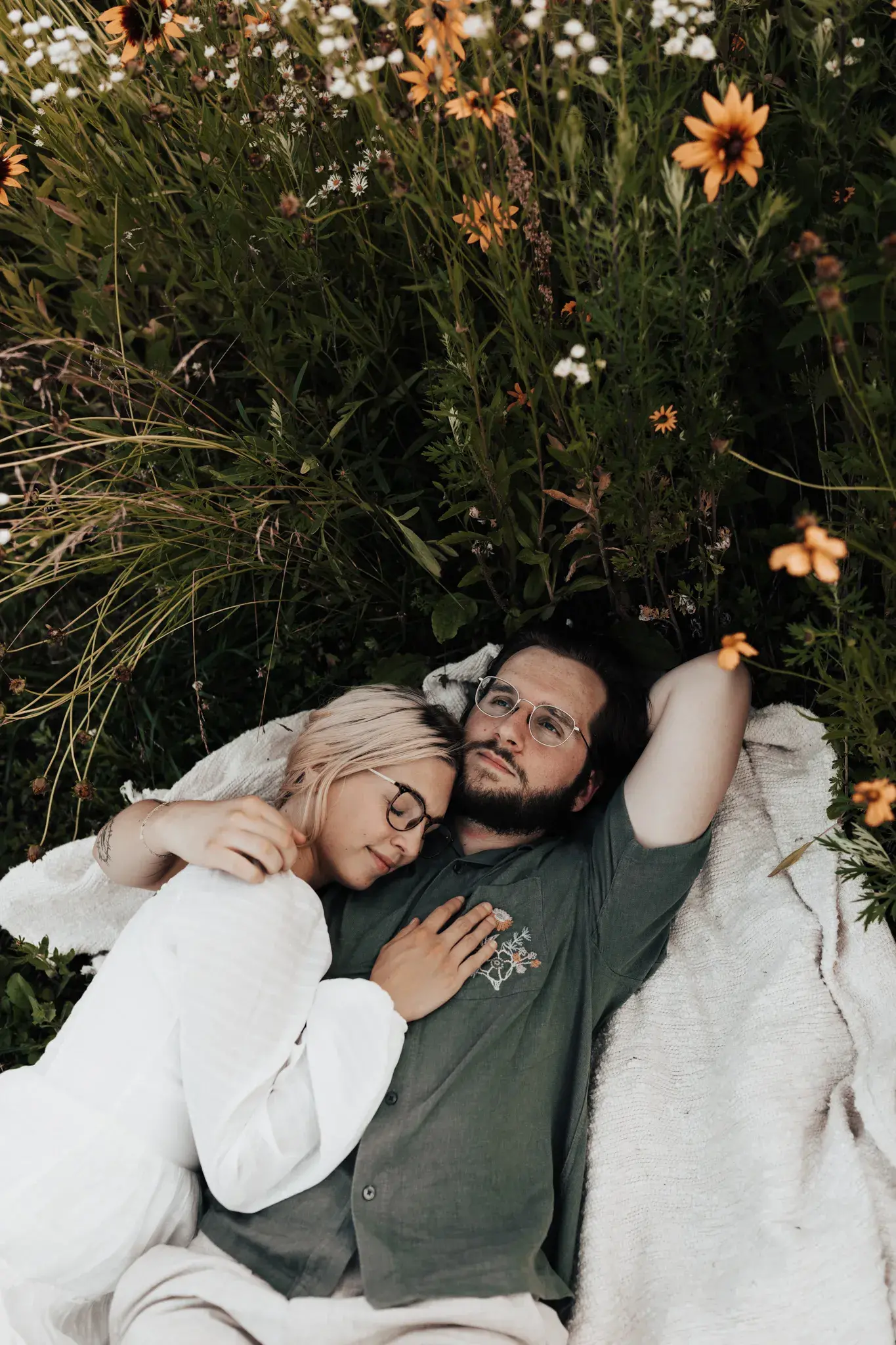 Couple relaxing together on a blanket in a wildflower meadow, sharing a quiet and affectionate moment surrounded by summer blooms.