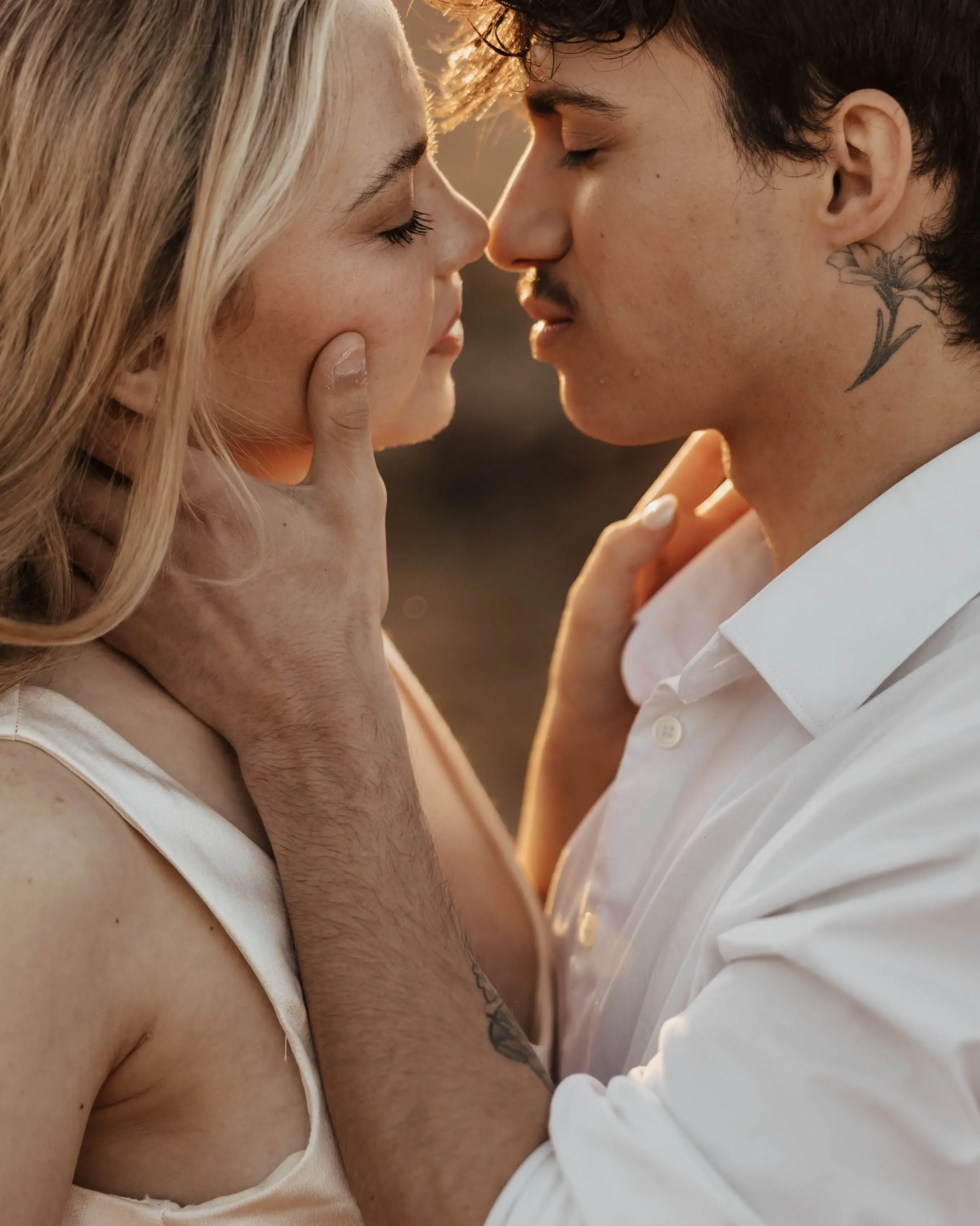Couple sharing an intimate close-up moment at golden hour, gently holding each other as warm sunlight glows between their faces.