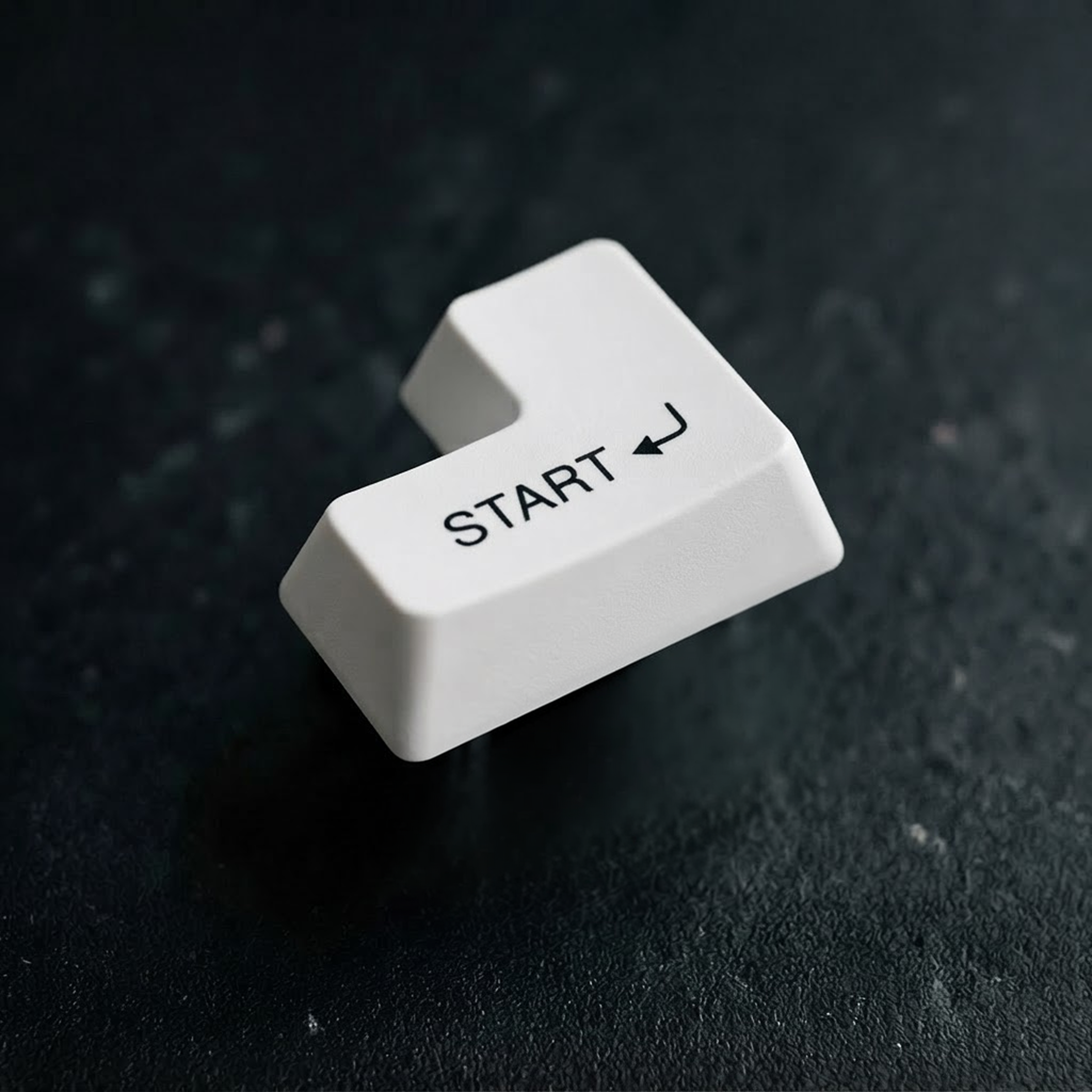 White Start keycap with a return arrow on a dark textured surface.