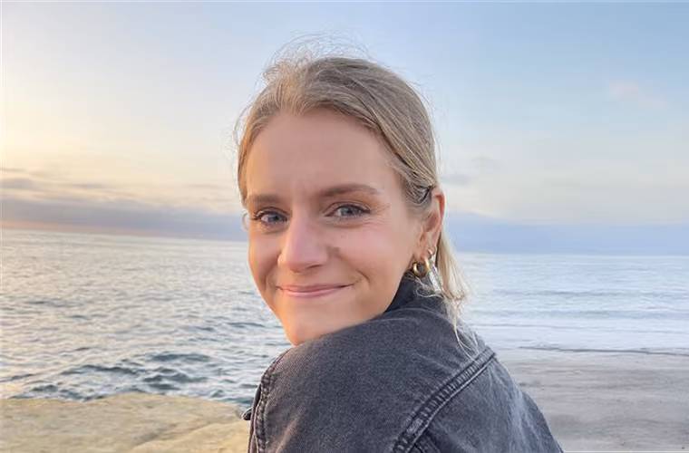 Smiling woman with blonde hair by the ocean at sunset.