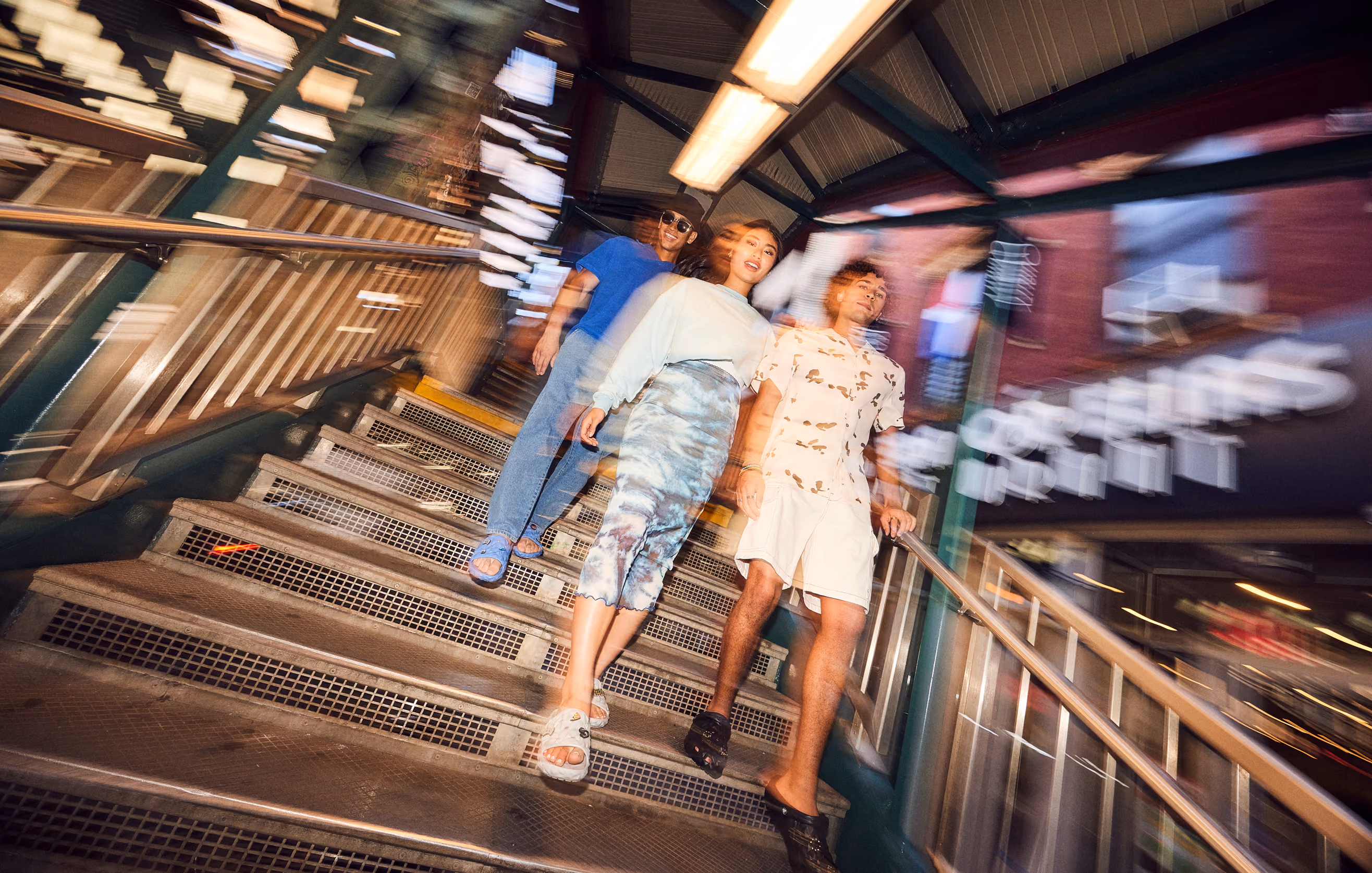 Three friends descending subway station stairs at night wearing Crocs sandals.