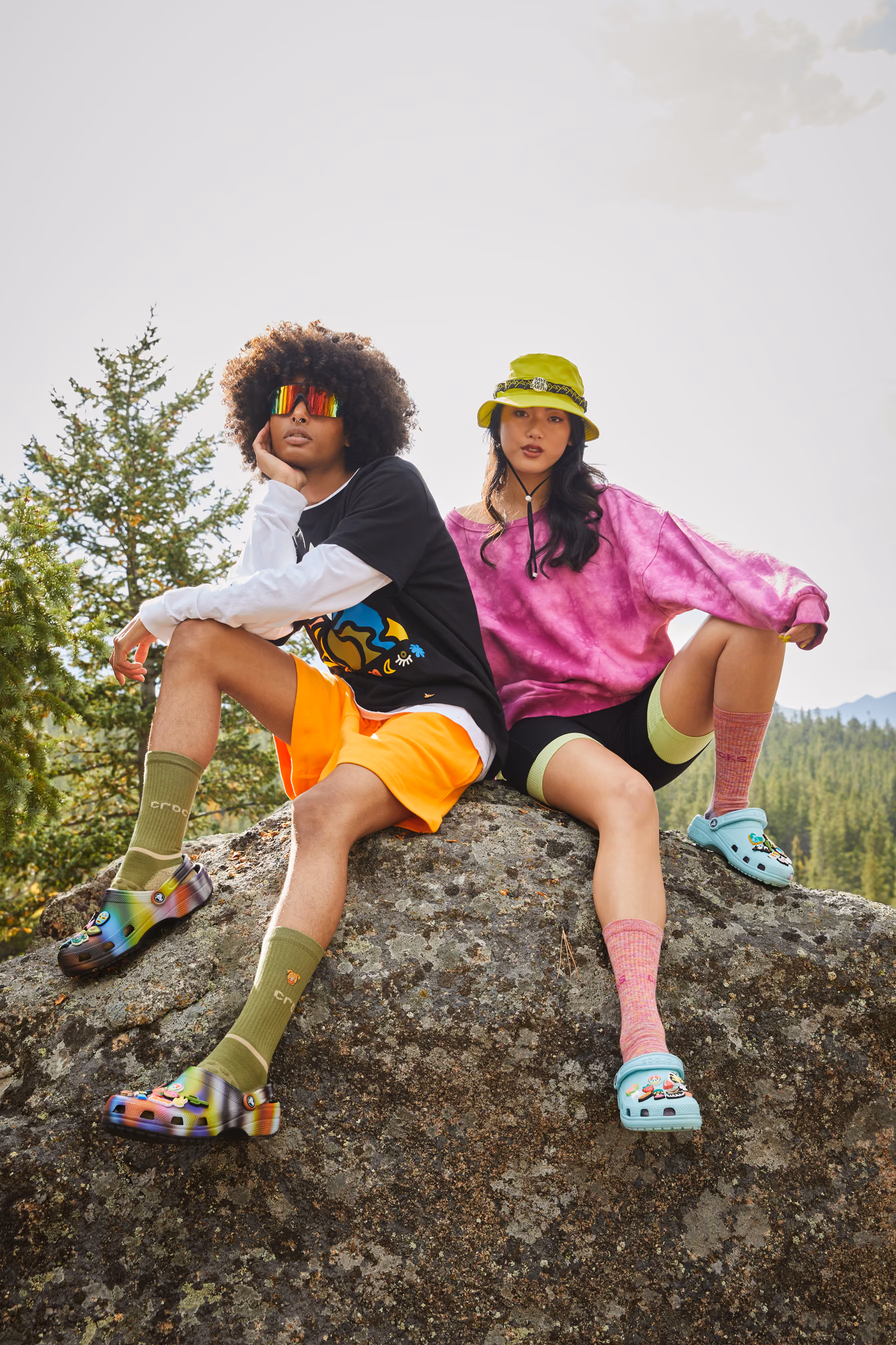 Two friends sitting on a boulder in the mountains wearing colorful Crocs clogs.