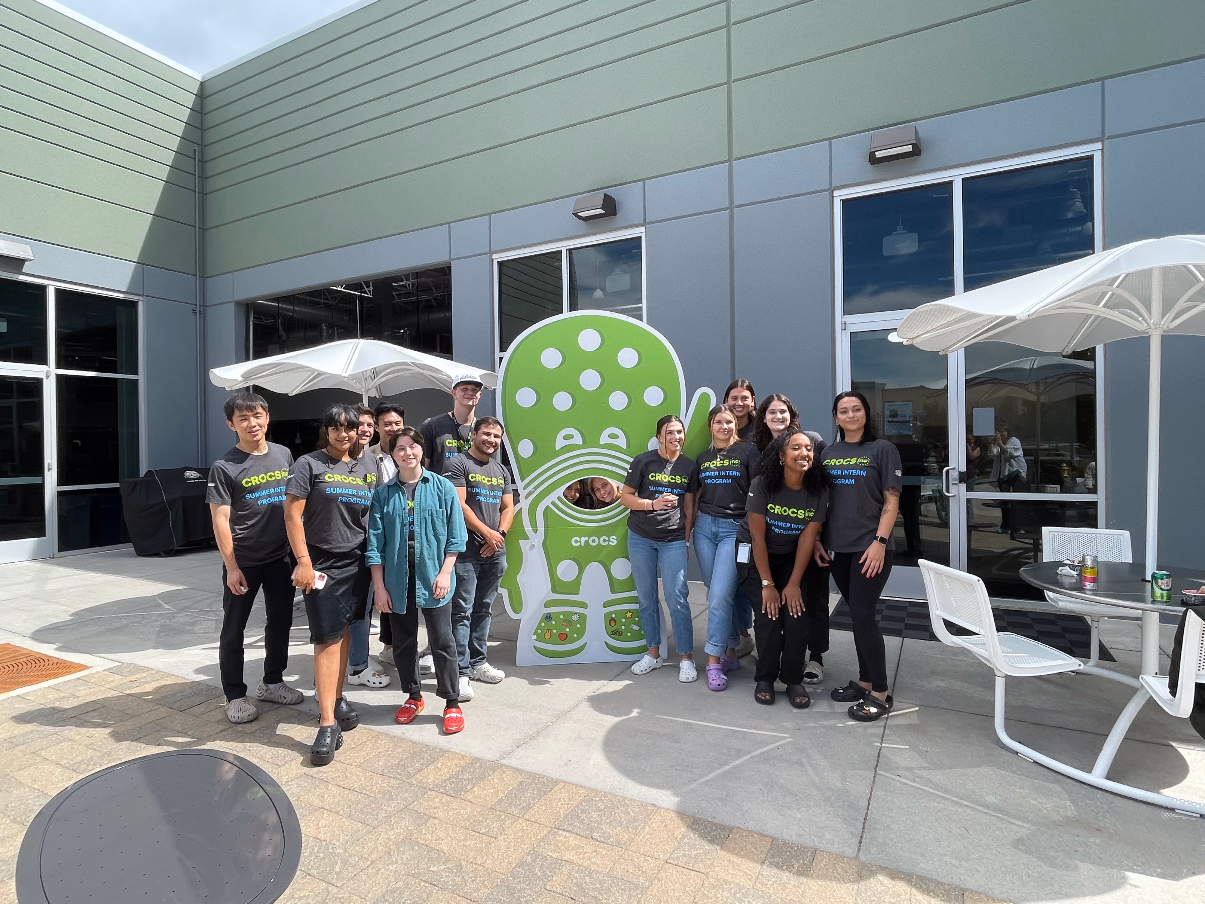 Group of Crocs interns posing outdoors beside a large clog-shaped sign.