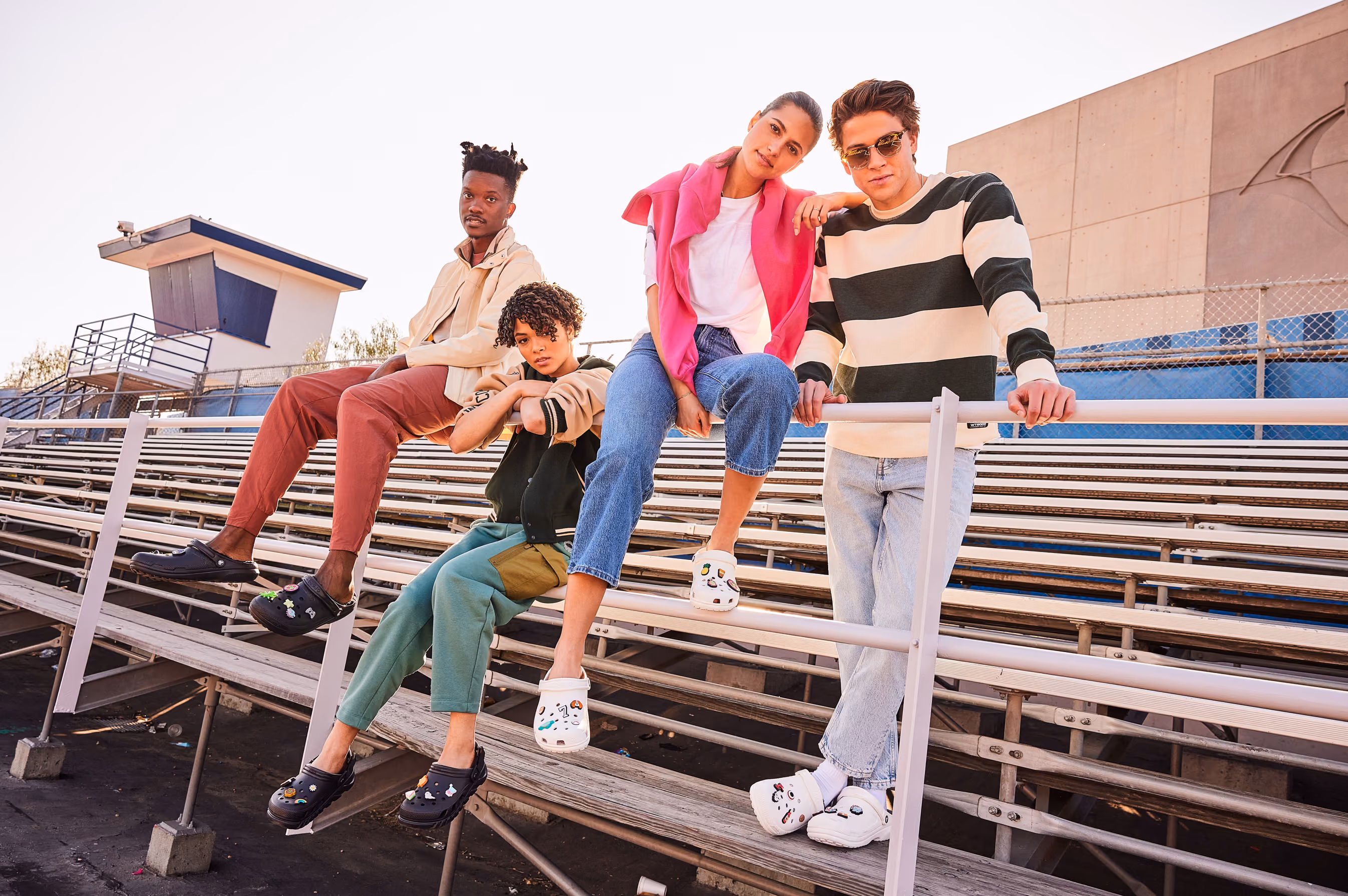 Four friends posing on stadium bleachers wearing Crocs clogs.