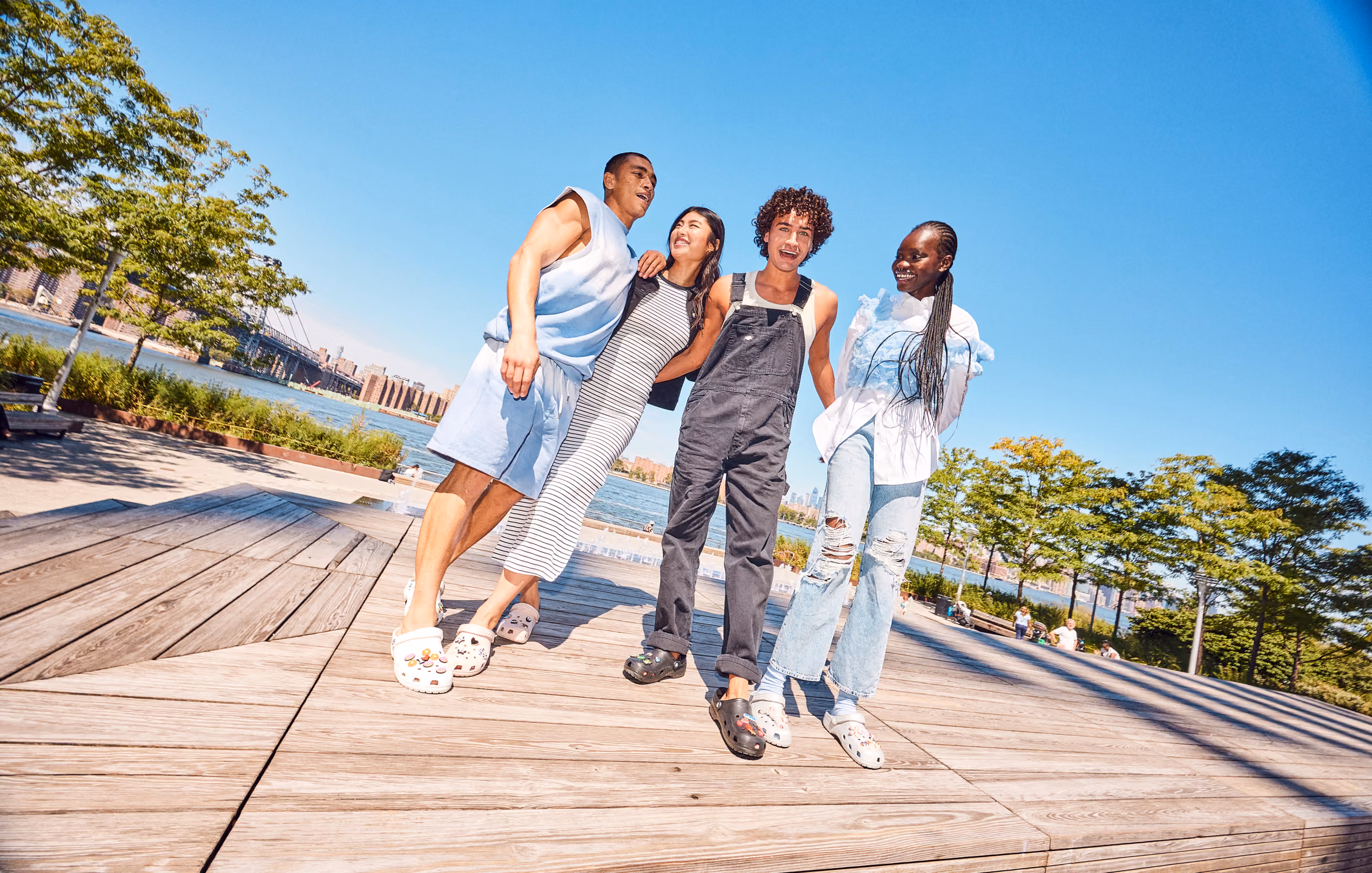 Four friends walking on a waterfront boardwalk wearing Crocs clogs and sandals.