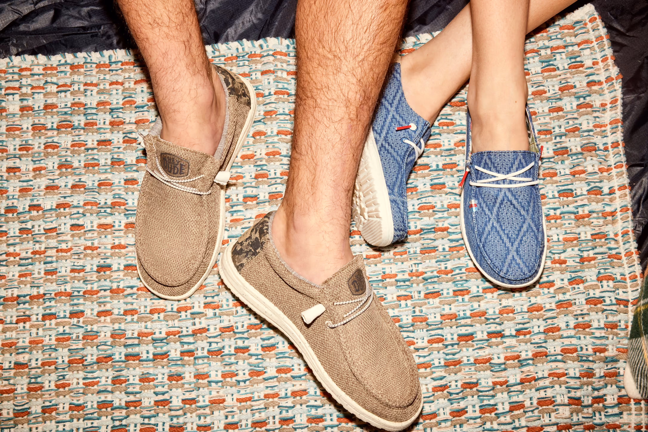 Close-up of tan and blue HEYDUDE slip-on shoes worn on a woven blanket.