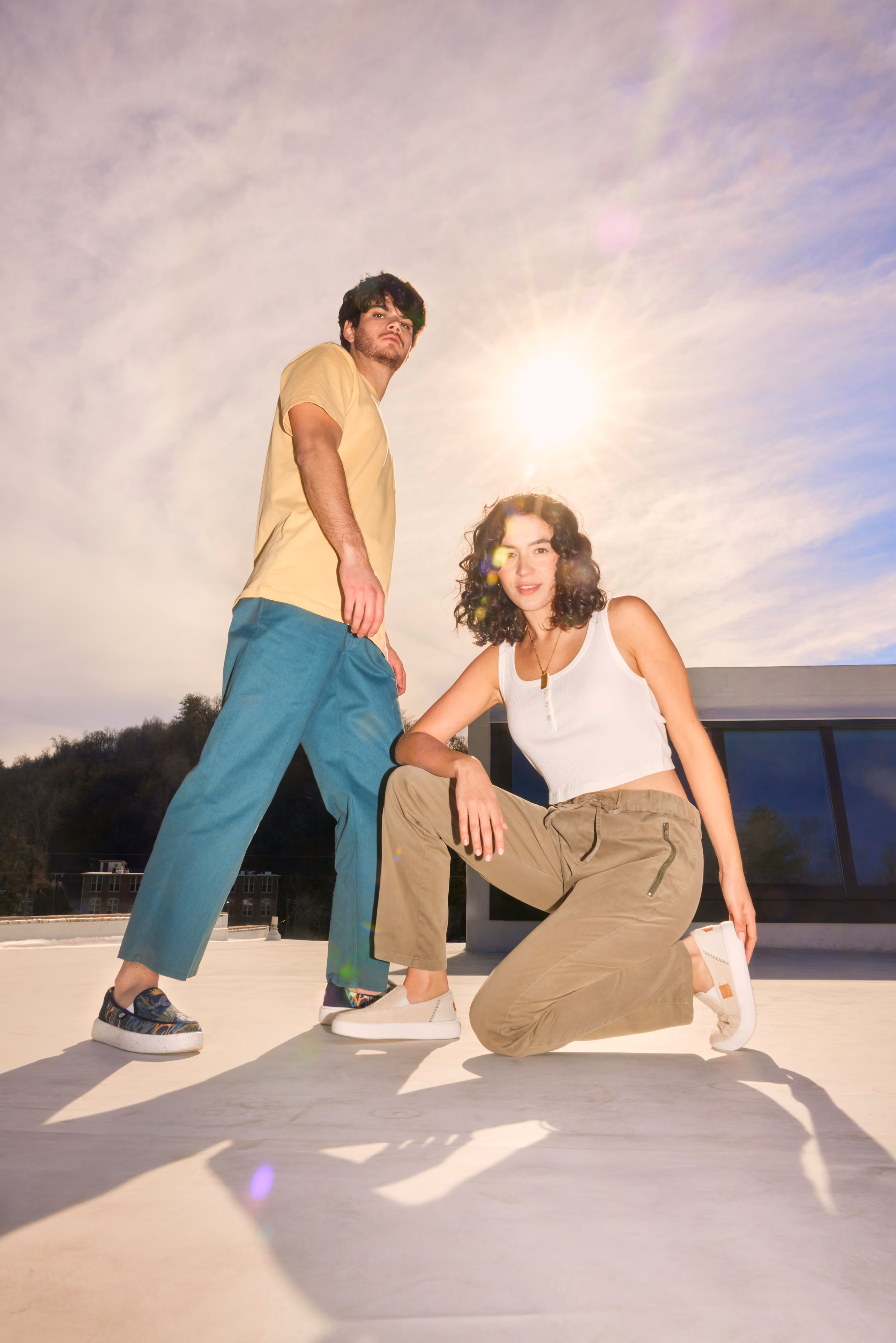 Man and woman posing on a sunlit rooftop wearing HEYDUDE shoes.