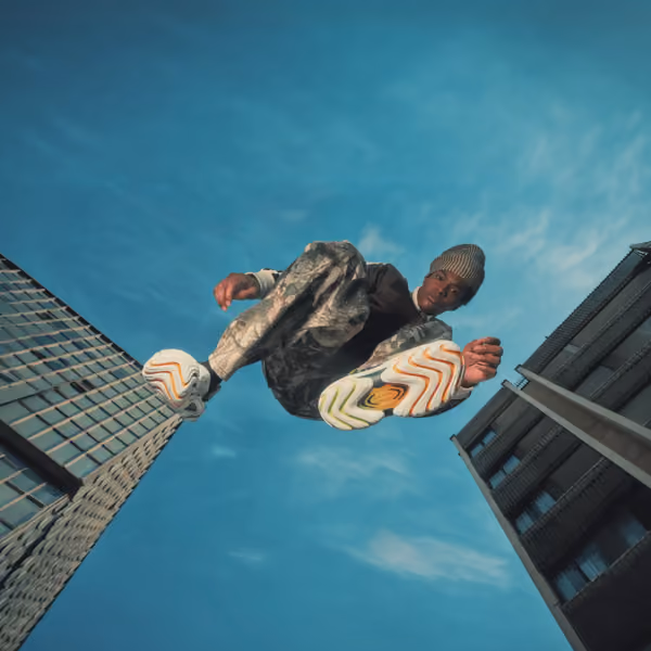 Person viewed from below between city buildings wearing colorful Crocs shoes.