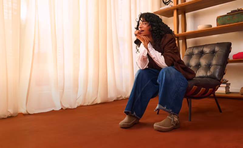 Woman seated in a living room wearing tan HEYDUDE shoes.