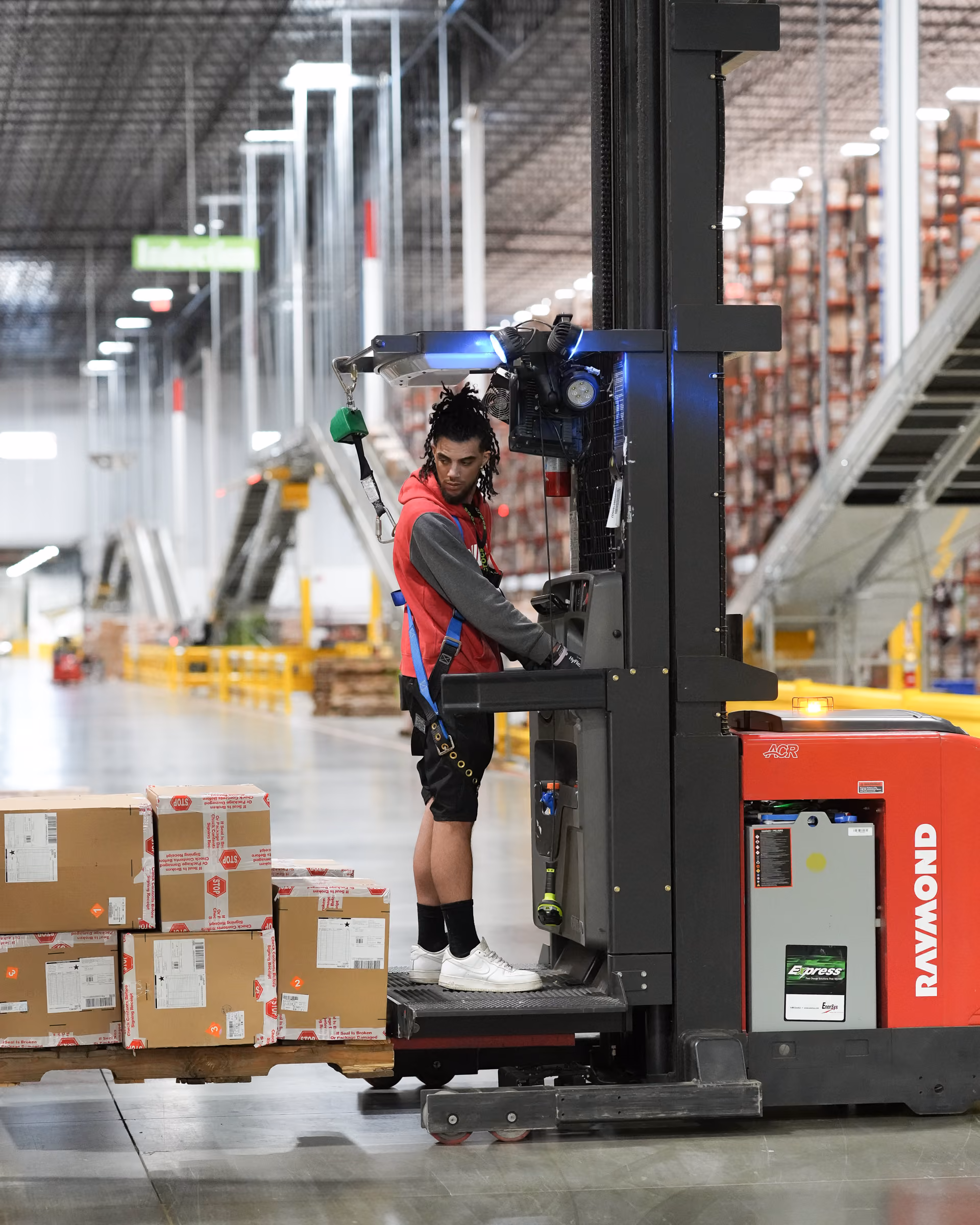 Employee operating a warehouse lift among stacked boxes.