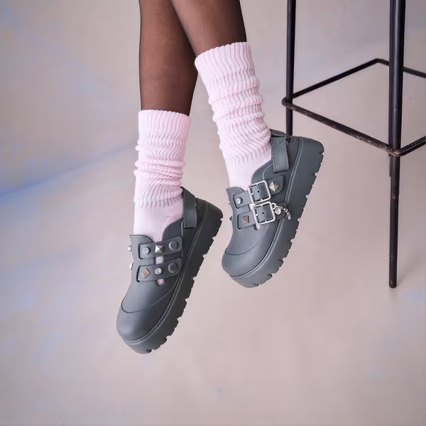 Gray platform Crocs clogs with buckles and studs worn with white leg warmers.