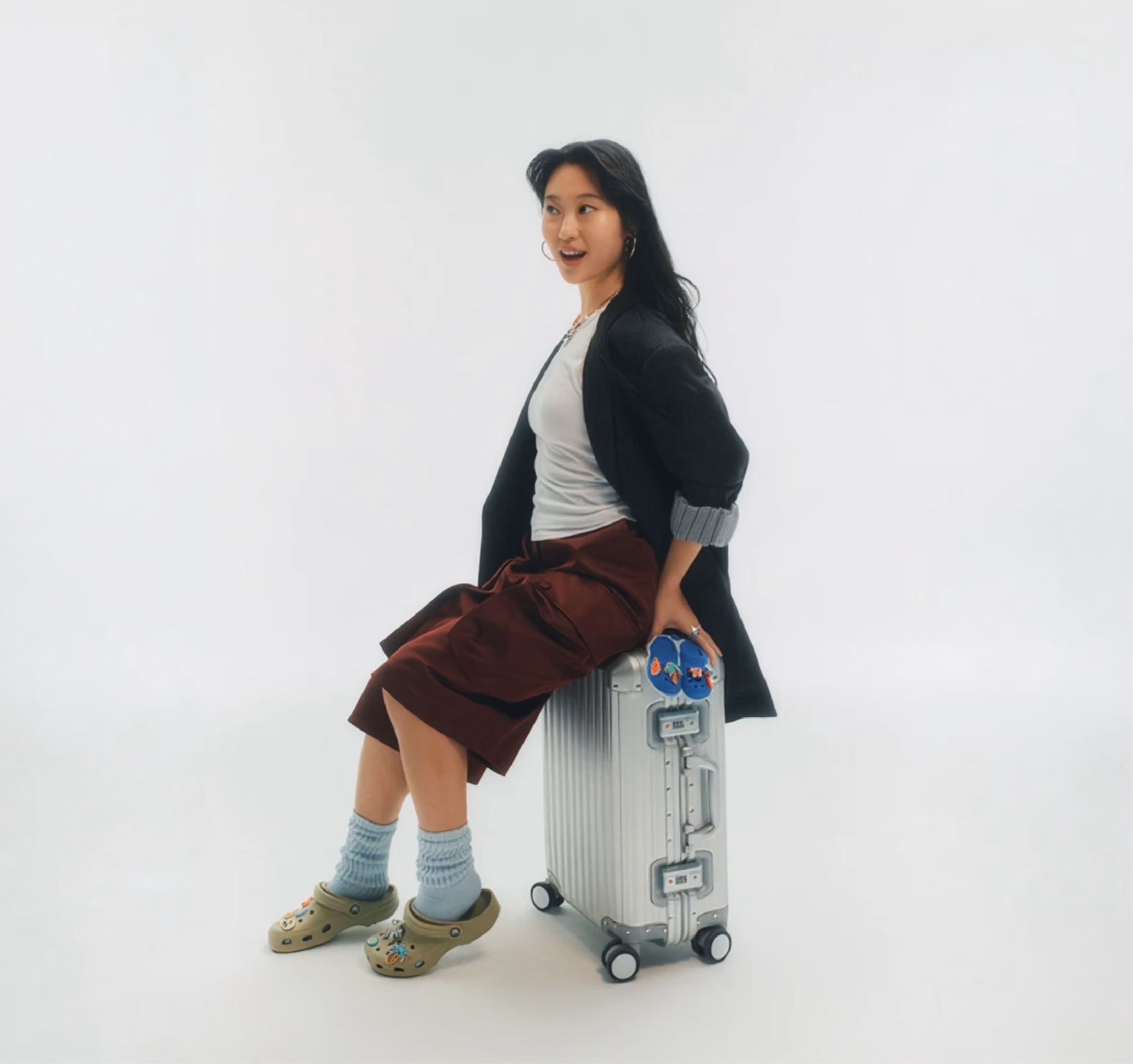 Woman seated on a silver suitcase wearing green Crocs clogs.