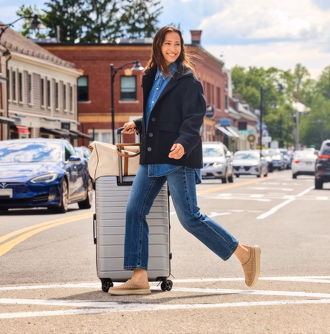 Woman rolling a suitcase across a downtown street.