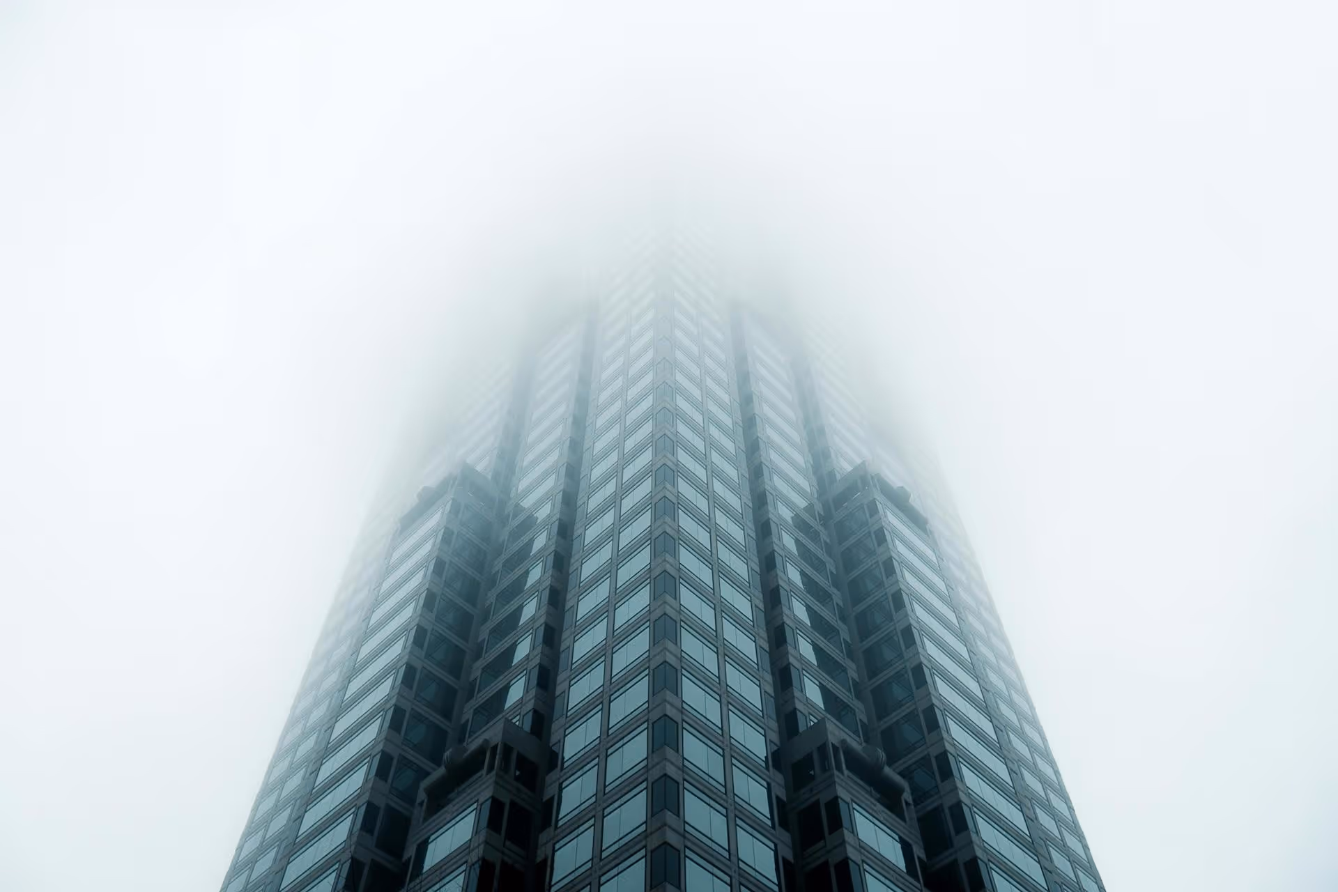 Modern skyscraper disappearing into fog, photographed from below with symmetrical glass facade architecture