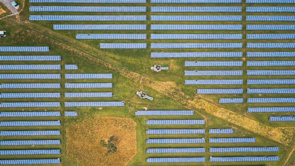Aerial view of solar panel arrays on grass fields with three small service vehicles.